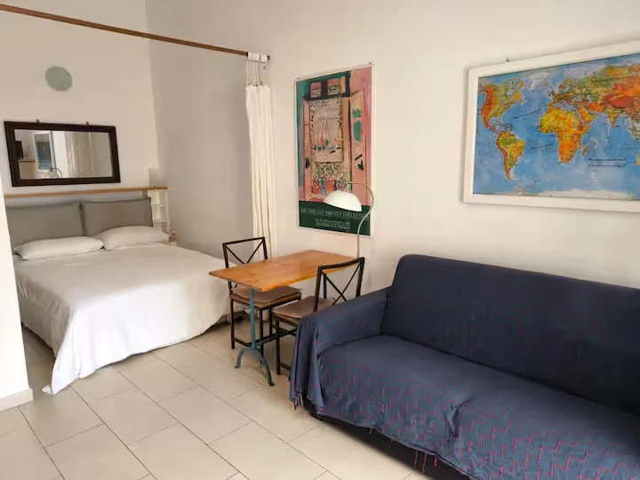 Interior de la casa con cama, sofá azul y mesa de comedor